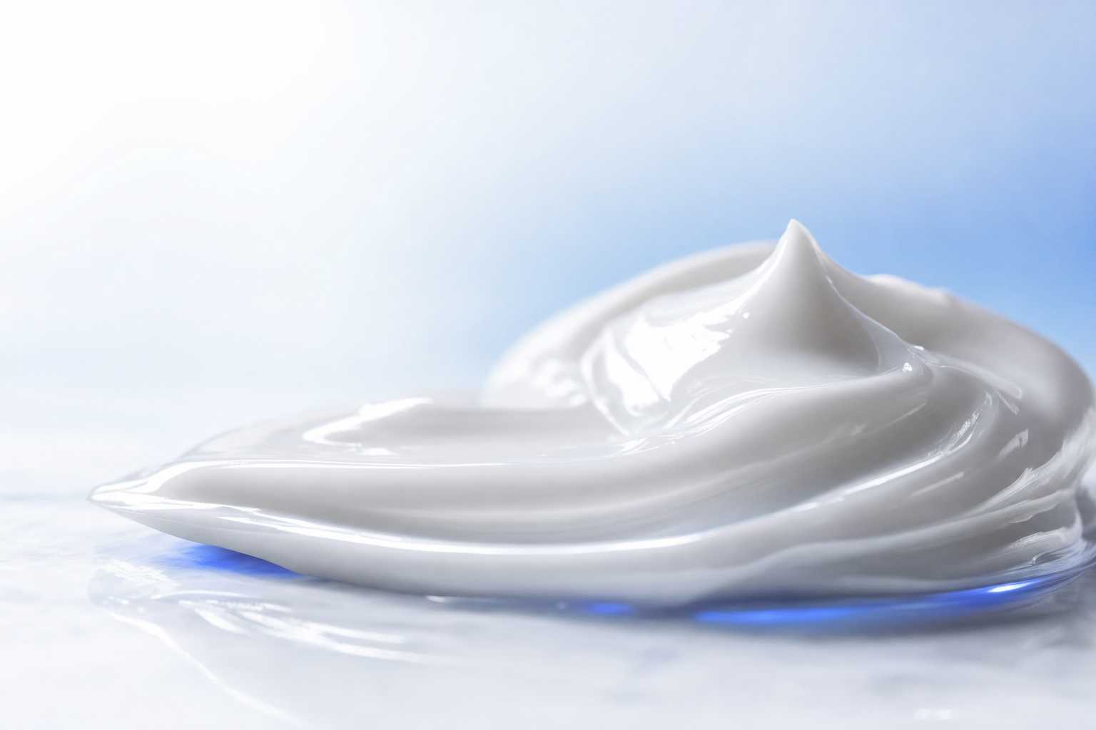 Premium macro of a smooth white cream swirled into soft peaks on a clean light surface with a cool blue accent