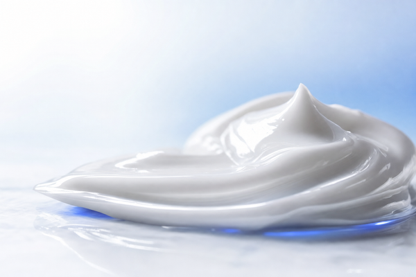 Premium macro of a smooth white cream swirled into soft peaks on a clean light surface with a cool blue accent